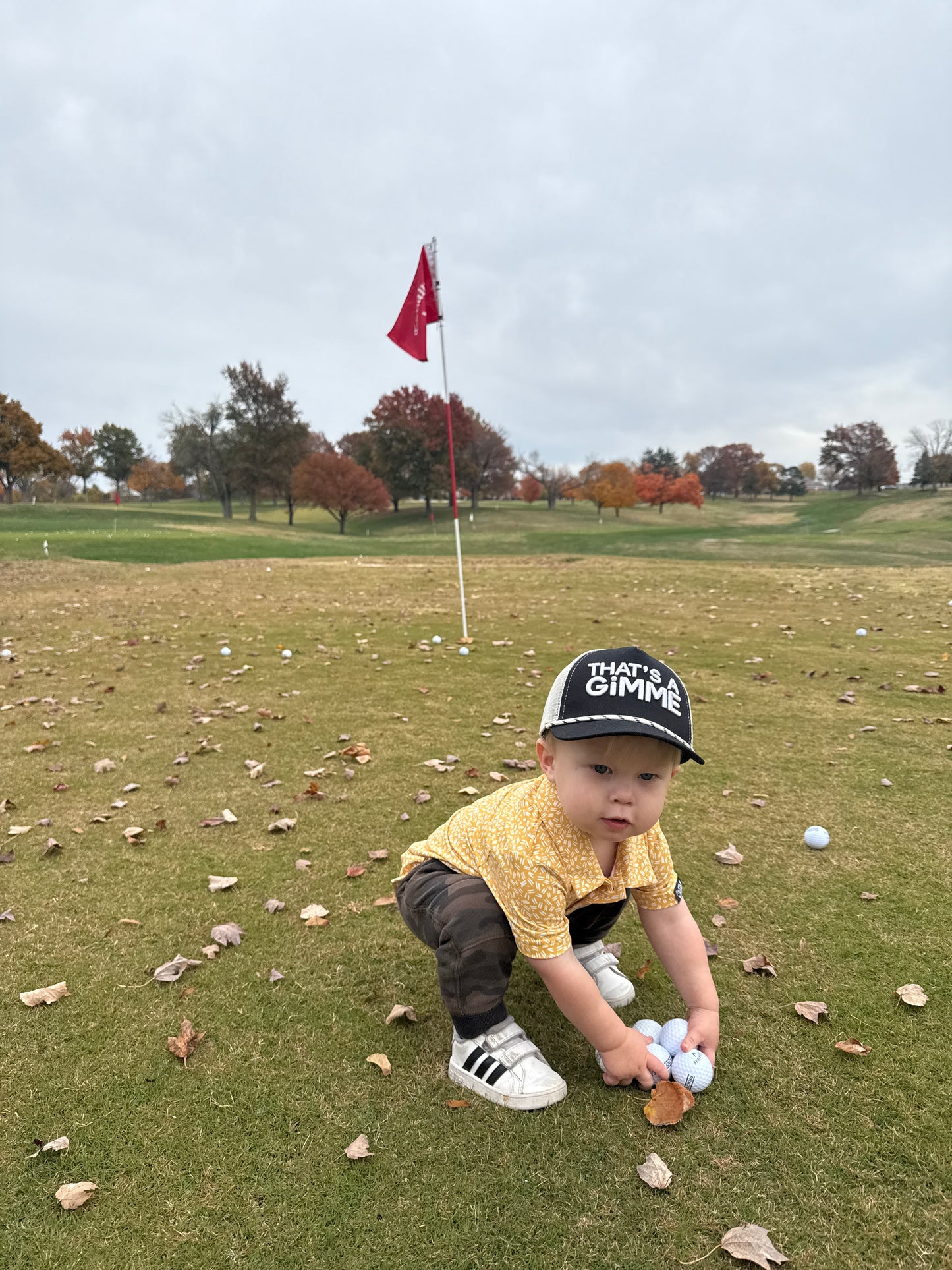 Toddler in that's a gimme hat picking up golf balls