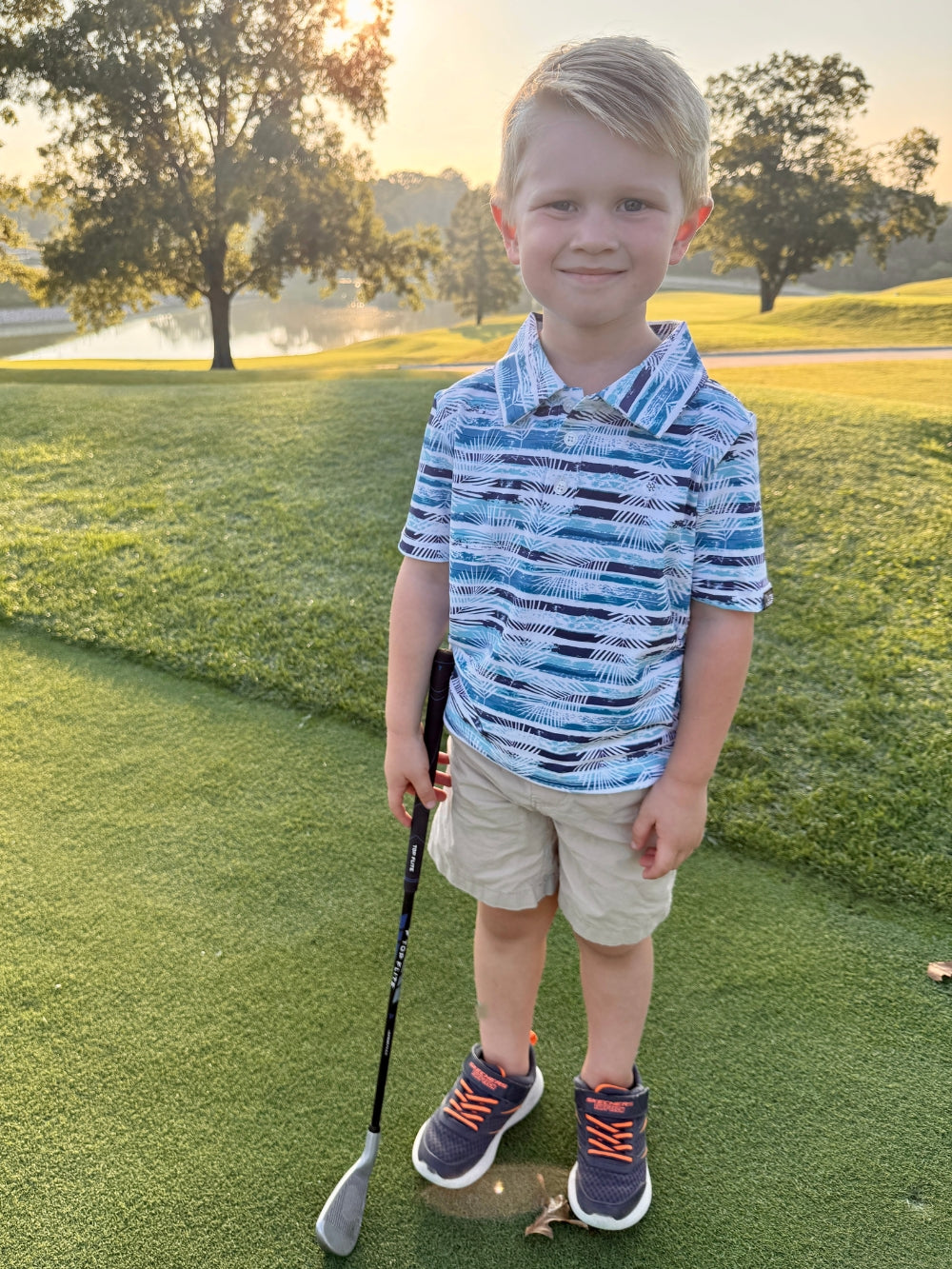 Young boy holding a golf club on a golf course at sunset