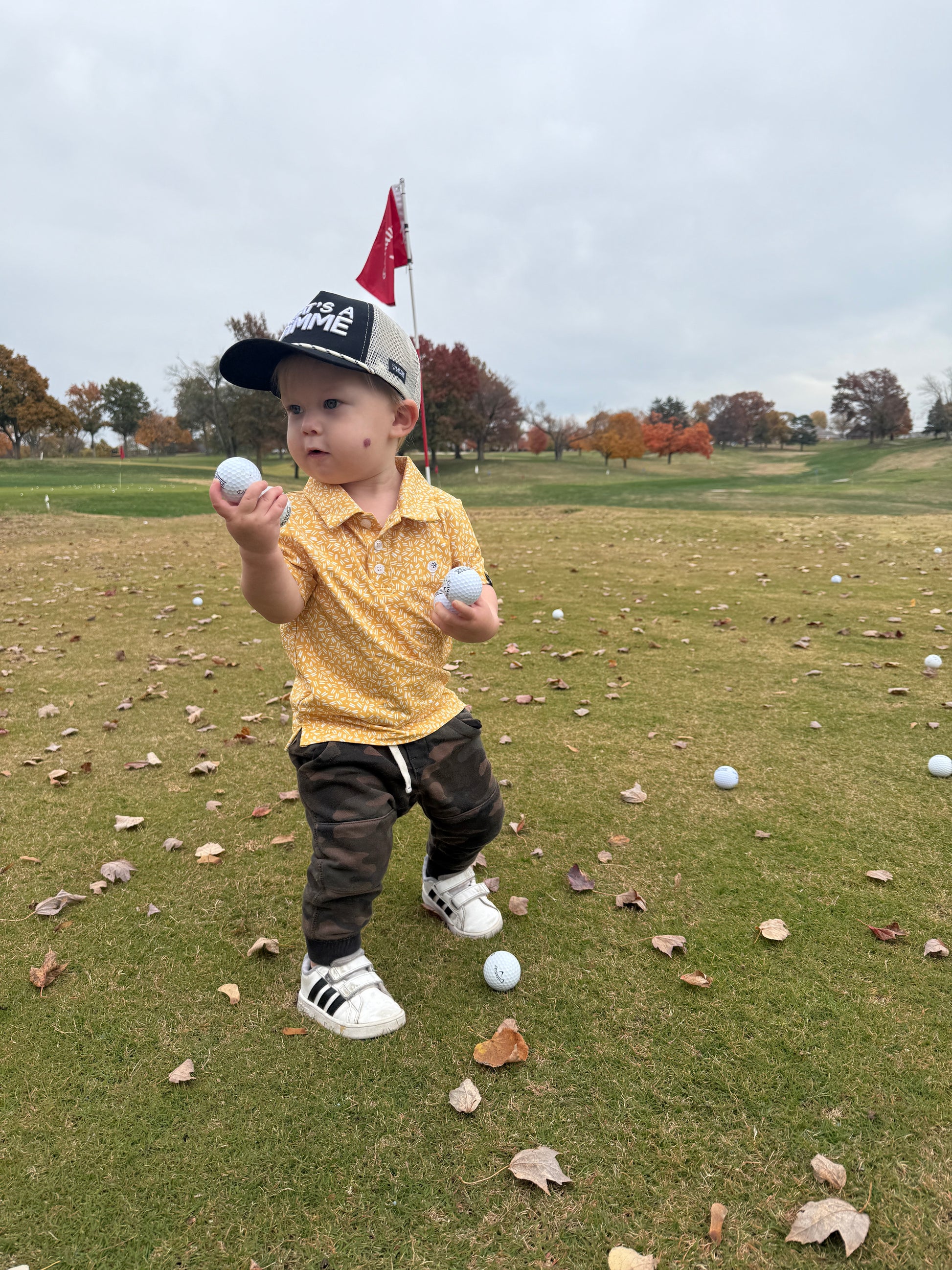 Toddler in that's a gimme hat holding golf balls